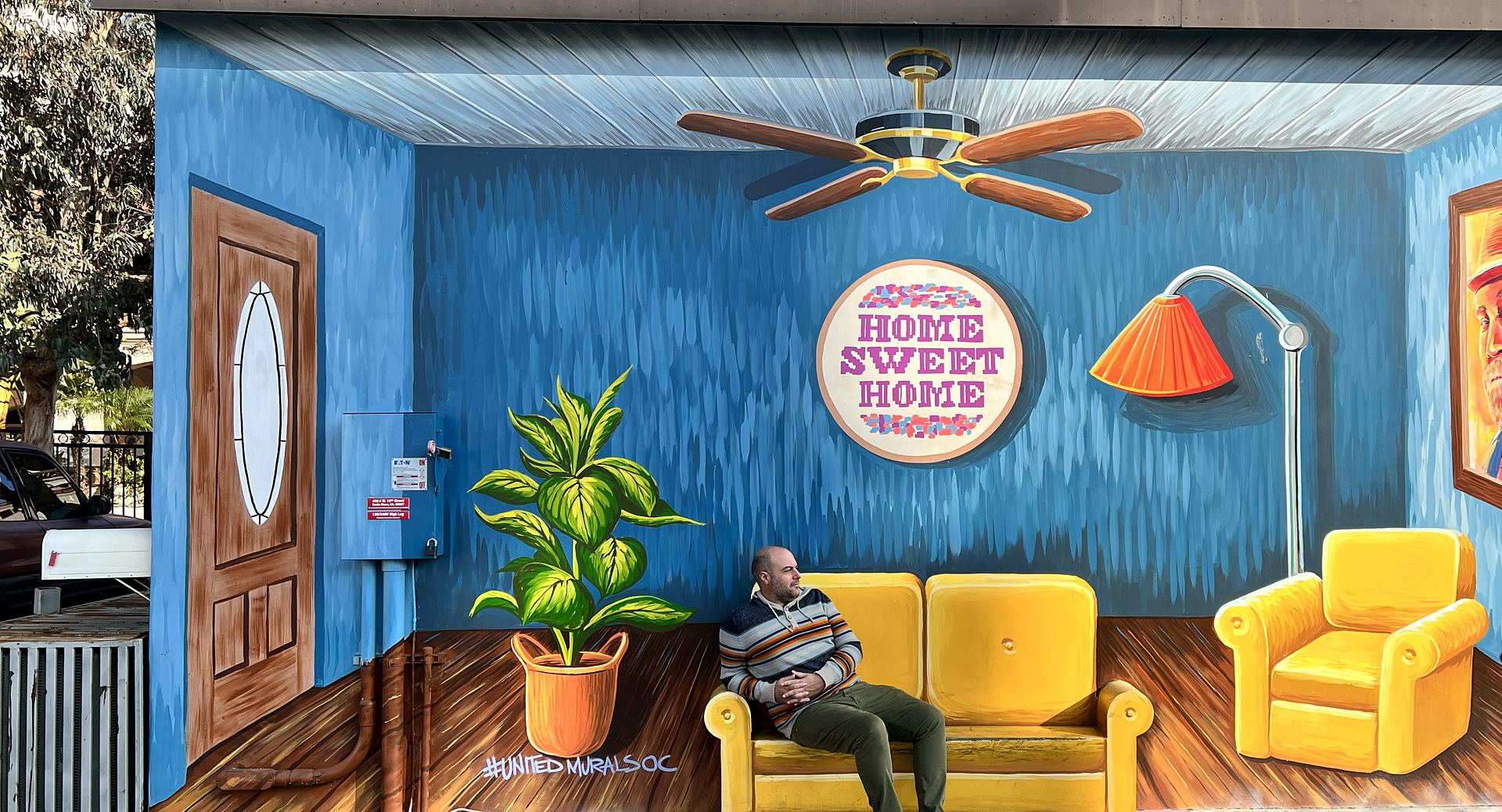 Jose Tizon sitting on a yellow sofa inside a painted street mural of a living room in Santa Ana, California